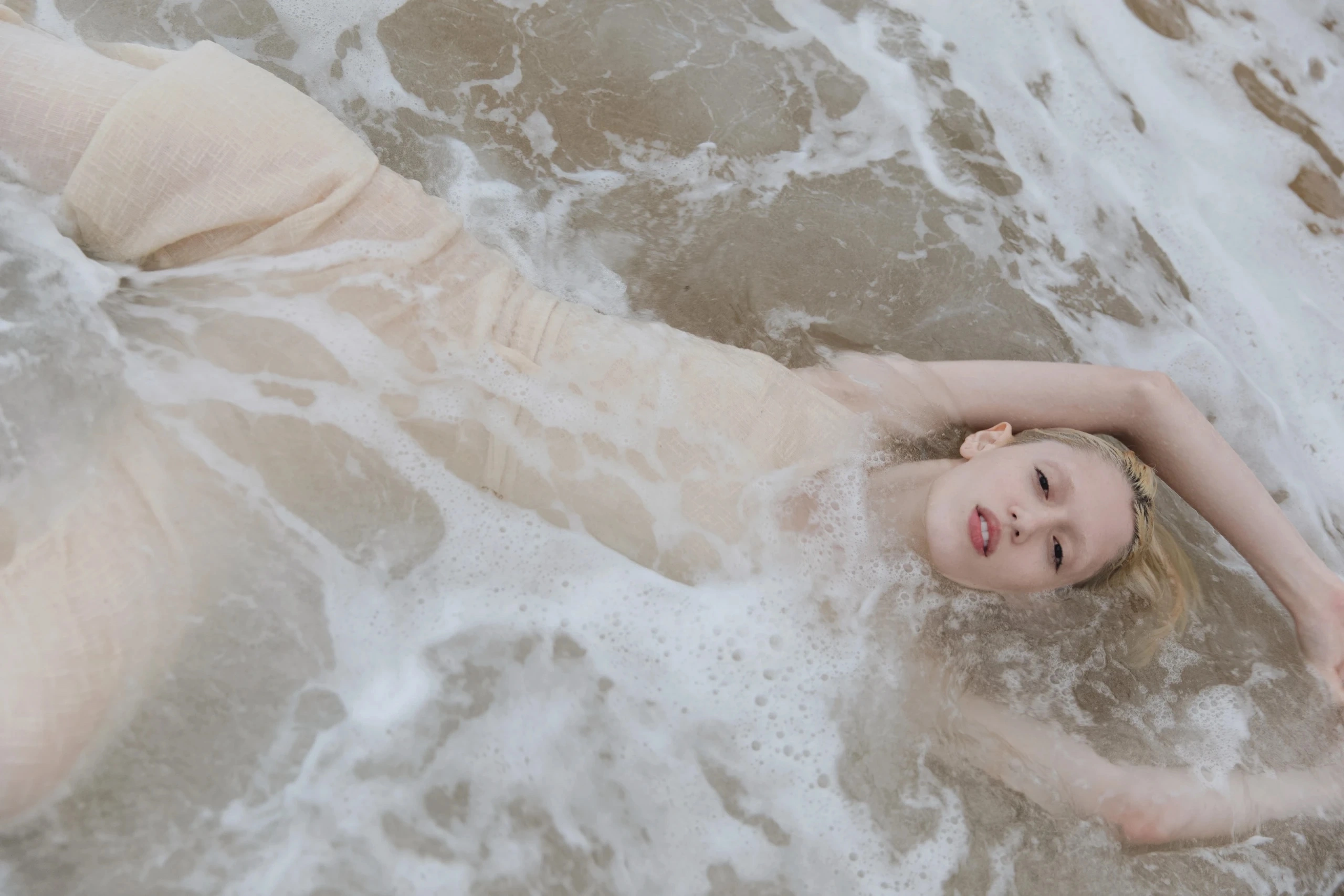 Model in a sheer dress lying in sea foam